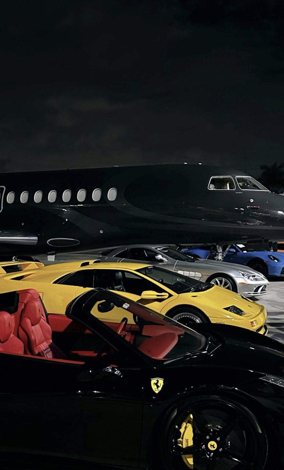 Exotic cars lined up in front of a private jet on the tarmac at night, Miami