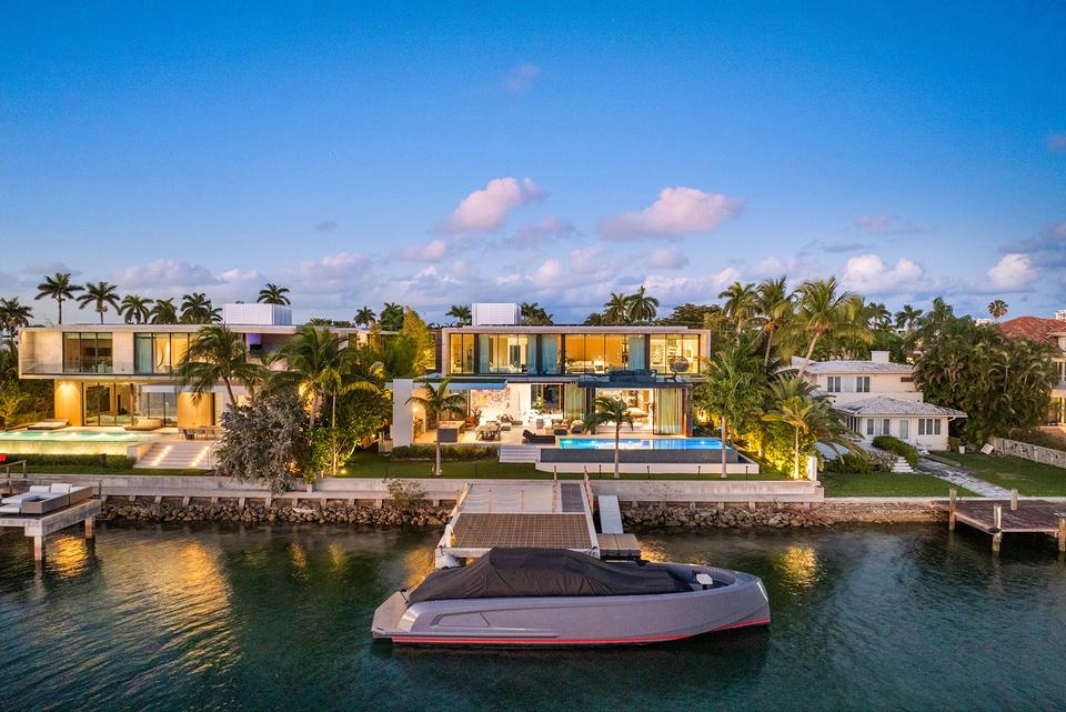Waterfront villa lit at dusk with a tender at the dock, Miami
