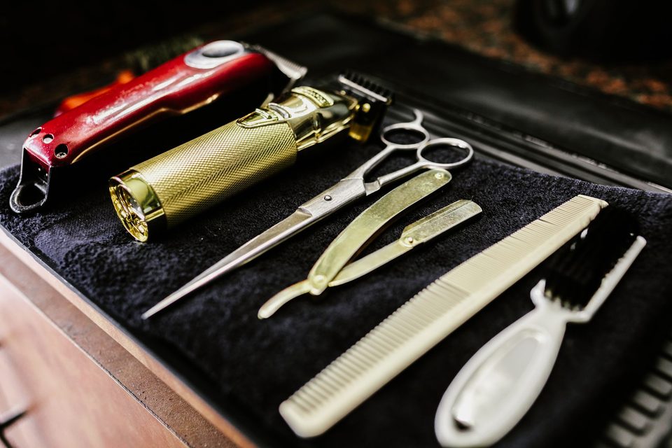 Gold barber clippers, scissors and razors on a black towel