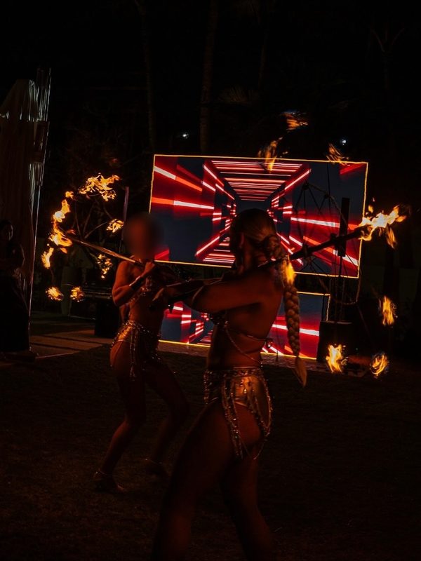 Fire dancers performing in front of an LED stage at night