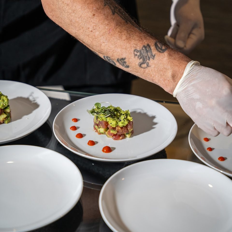 Gloved hands placing a plated tartare course
