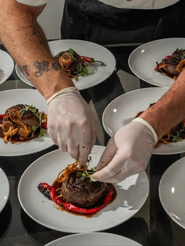 Chef in gloves finishing plated dinner courses