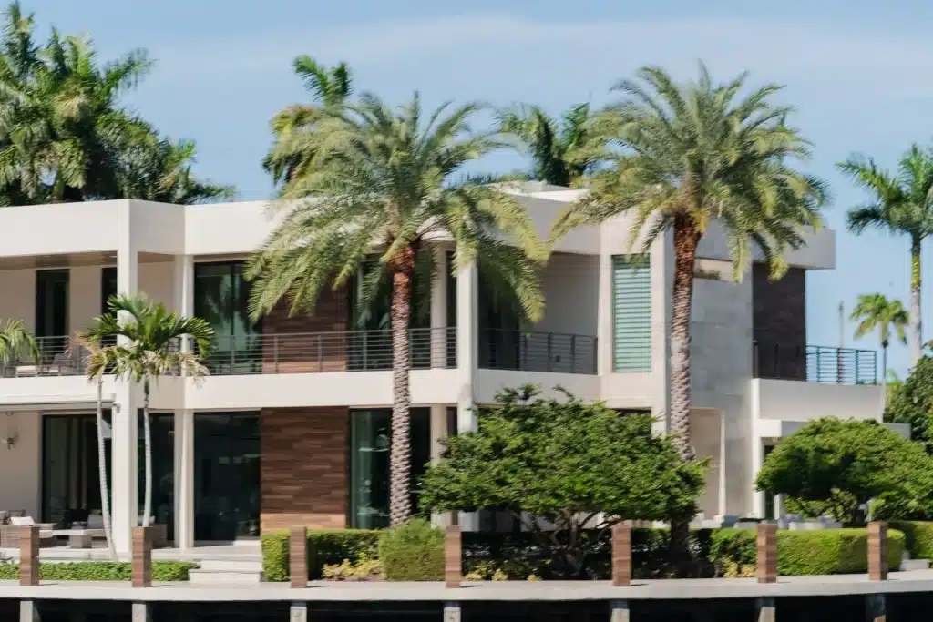 Modern waterfront villa with tall palm trees and a private dock on calm water