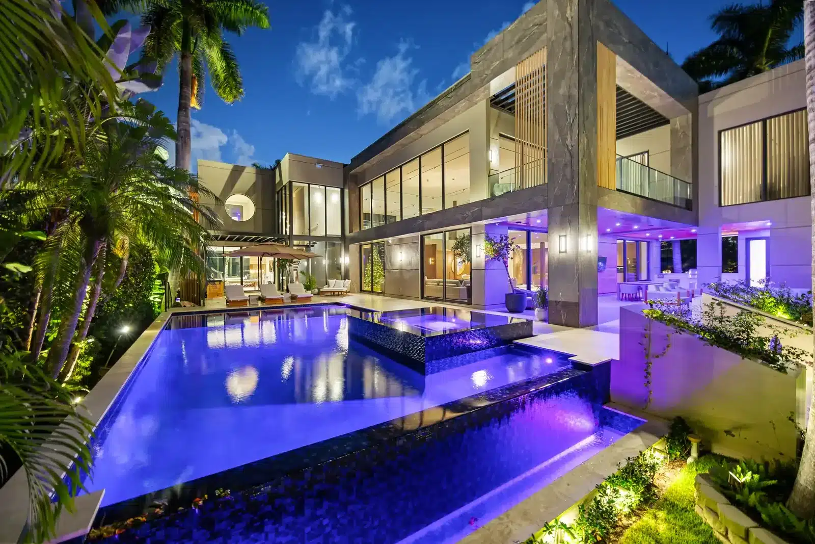 Modern villa at dusk with a lit pool and palm trees on Belle Meade Island in Miami