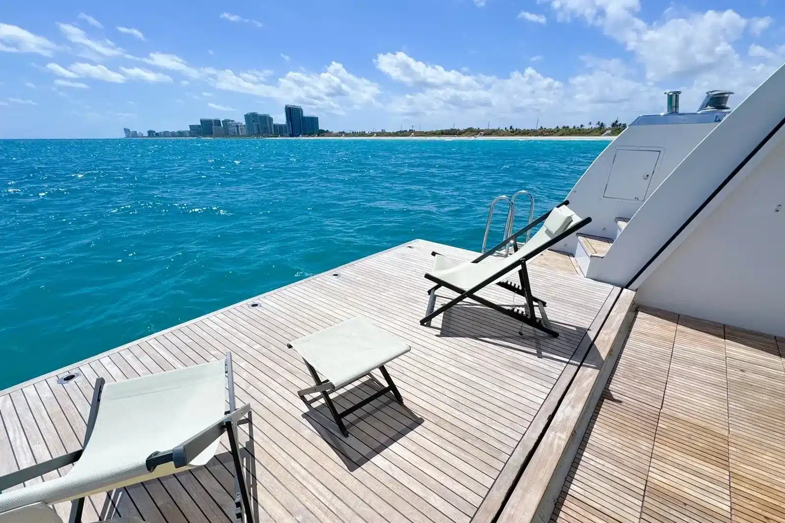 Swim deck with deck chairs on the 112 foot WHS Marine yacht off Miami Beach, turquoise water and the coastline behind